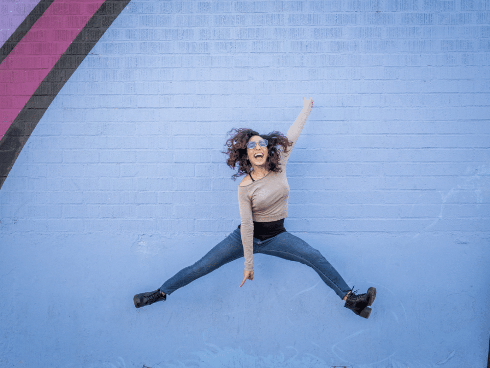 young hispanic woman jumping in front of a mural with a positive attitude